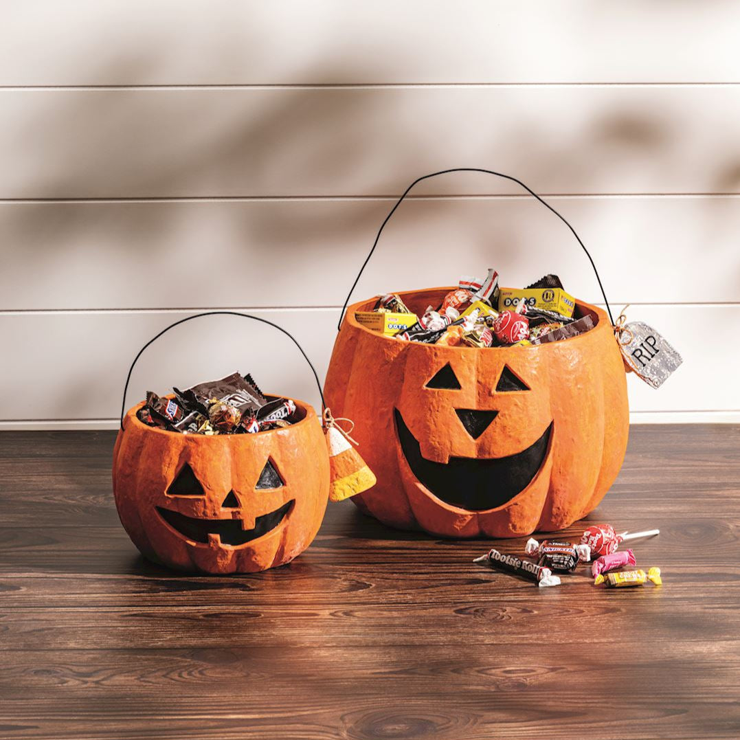 Two Halloween candy buckets with jack-o'-lantern faces on a wooden surface.